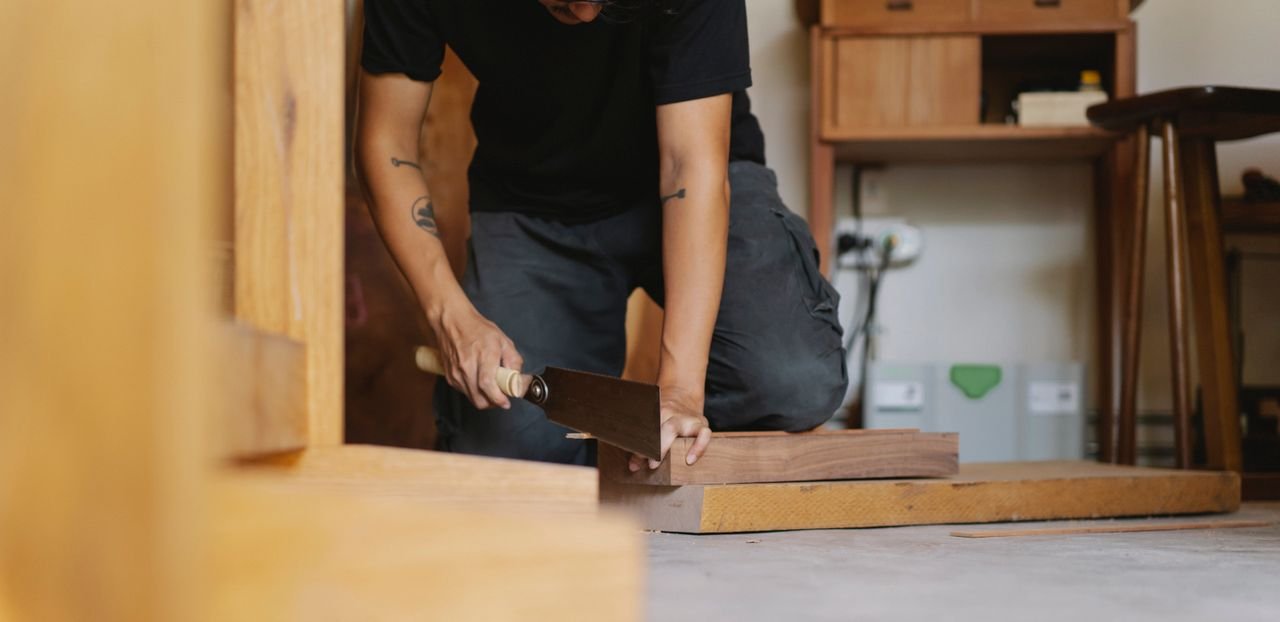 Crop anonymous male carpenter in casual clothes using flush cut saw while creating wooden object in workshop in daylight