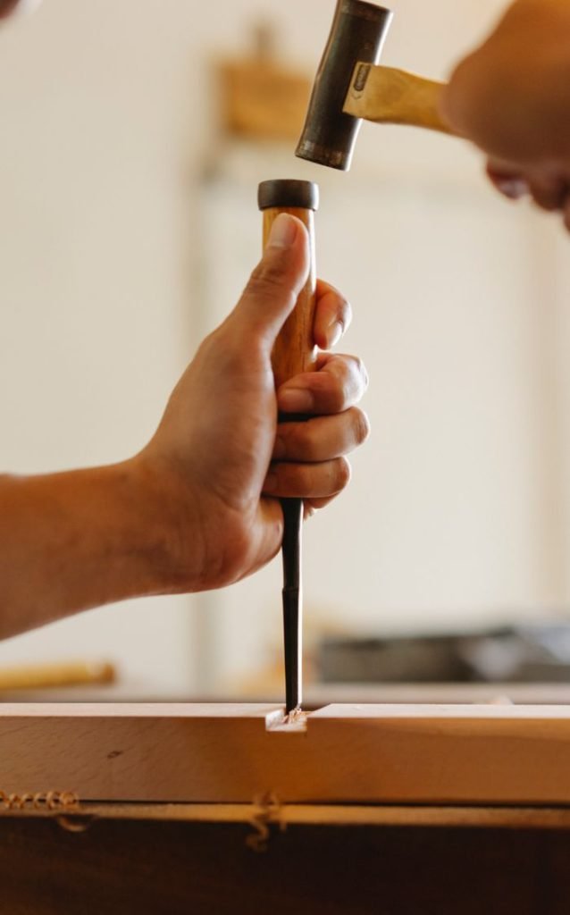 Crop unrecognizable male carpenter working with chisel and hammer while creating wooden object in workshop
